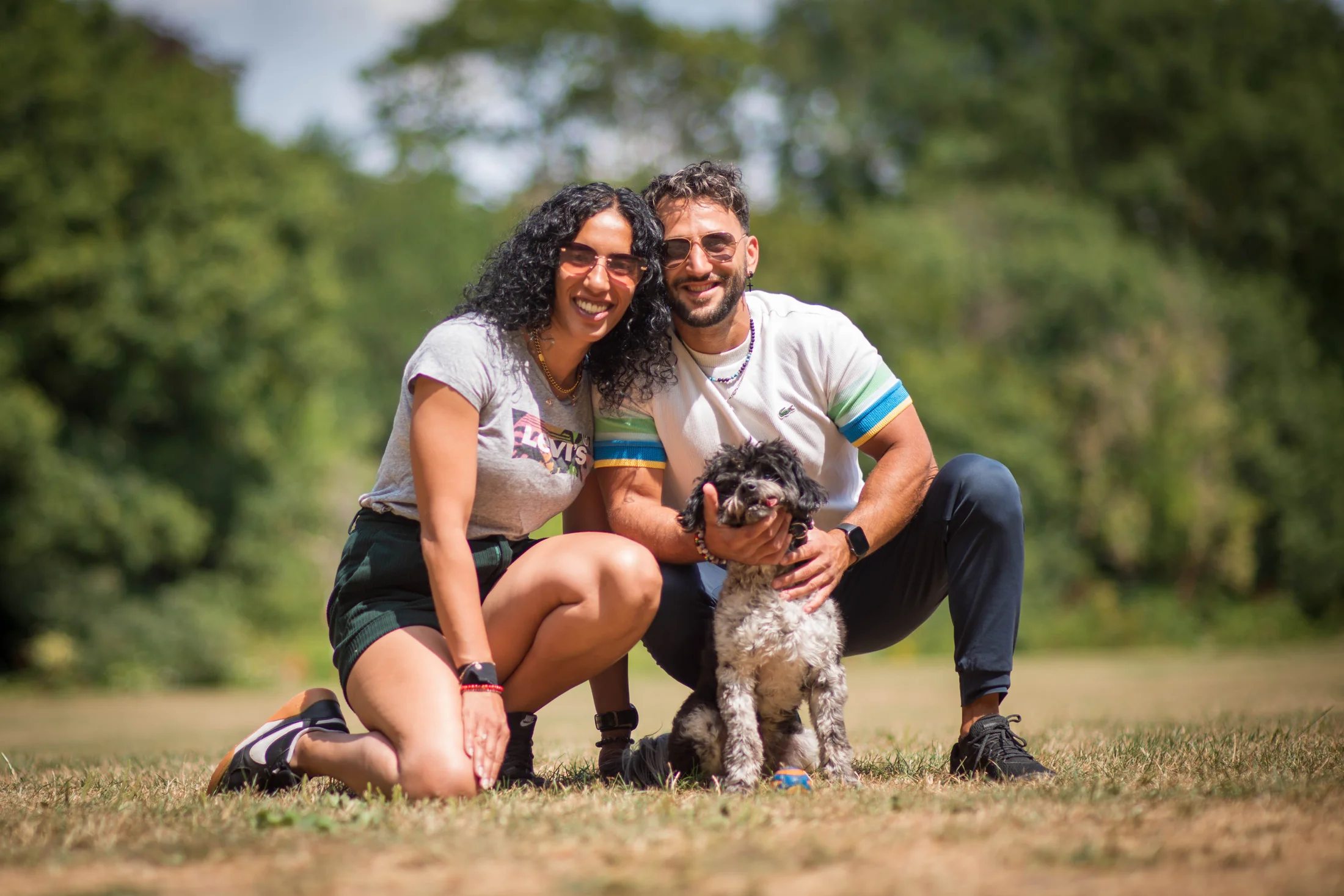 A smiling couple posing with their dog in a London park