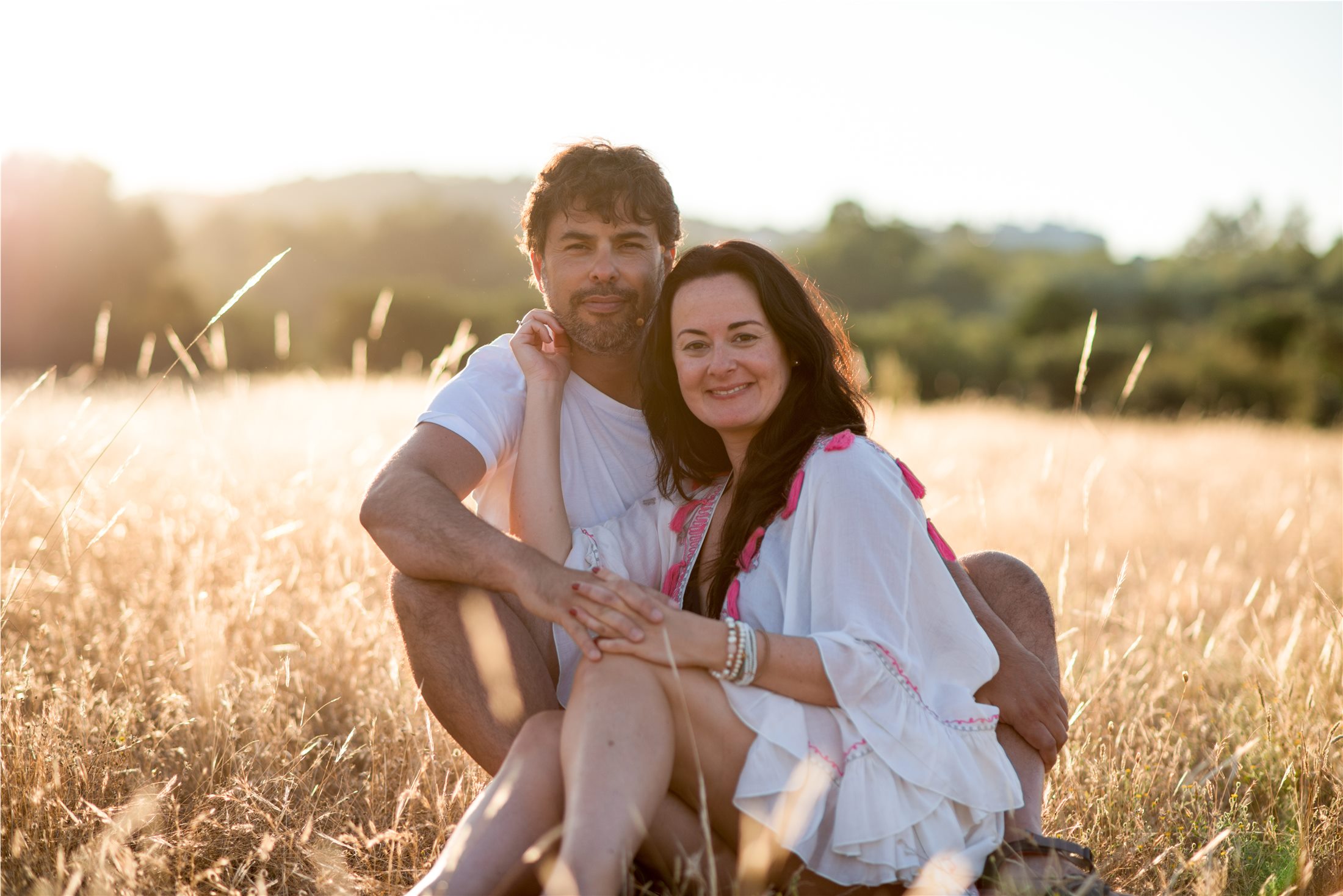 A couple sitting closely together in a field at golden hour