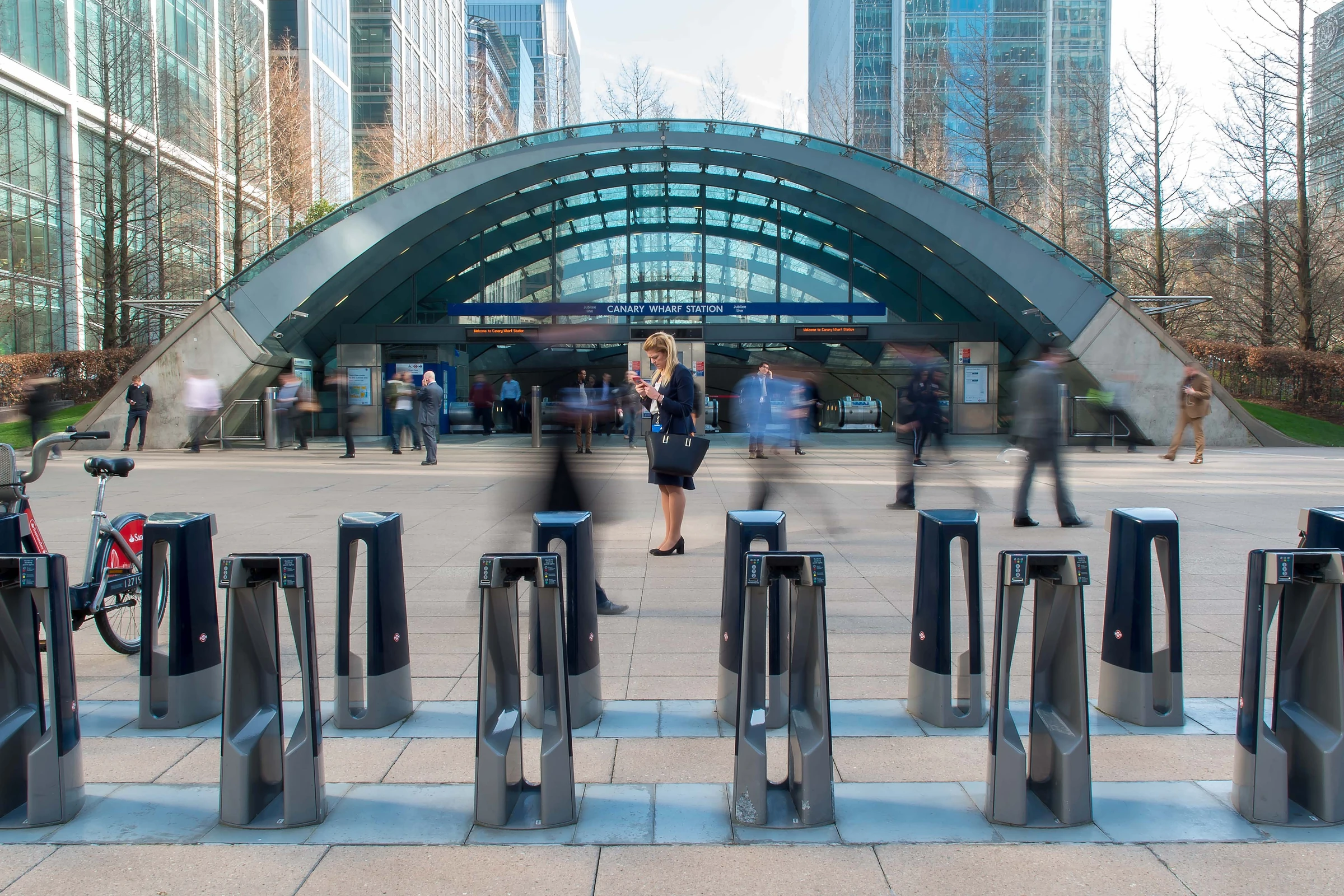 A woman standing still among blurred commuters outside Canary Wharf station