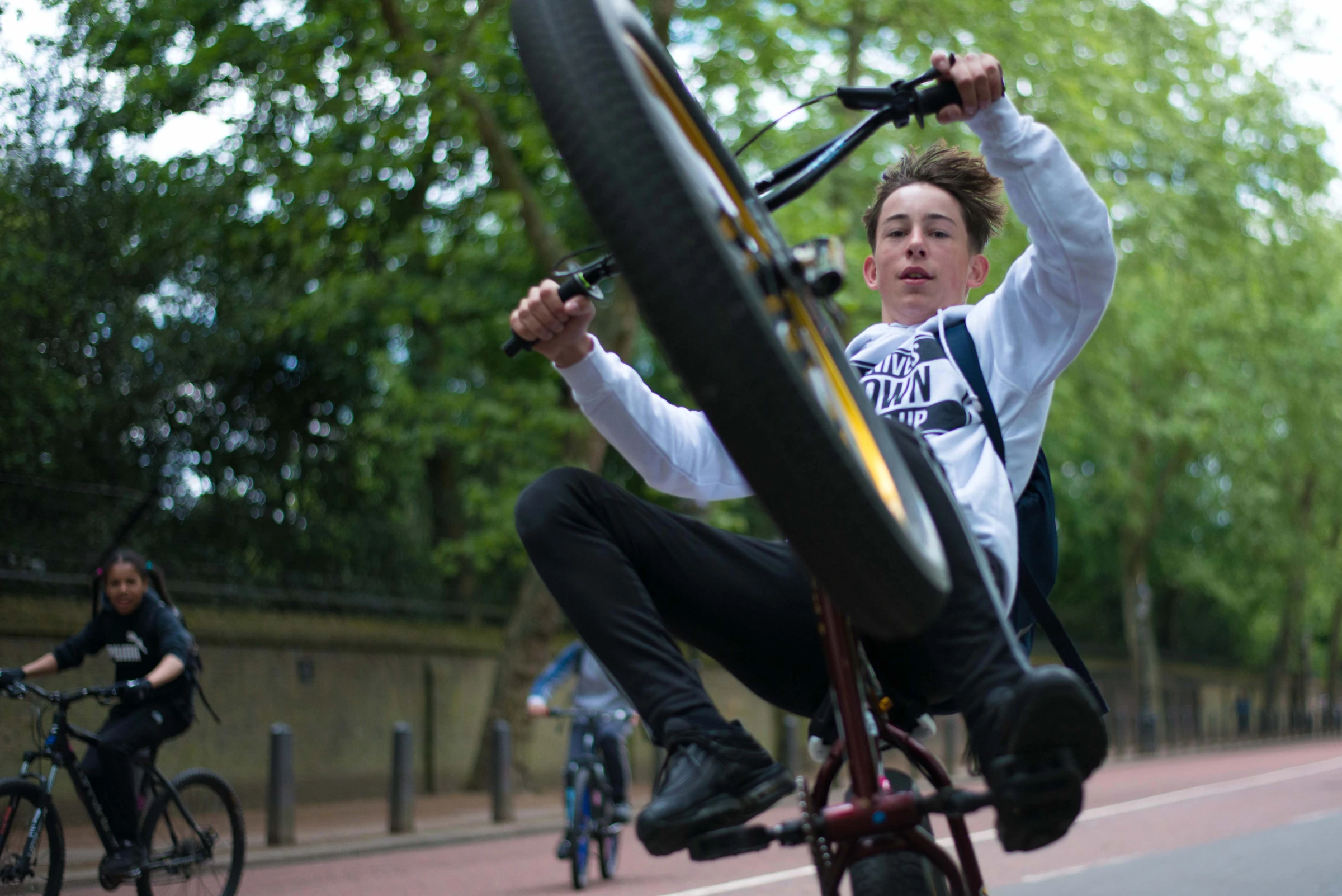 A young cyclist lifting his front wheel towards the camera on a London cycle path