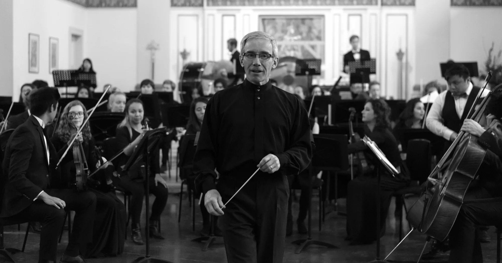 A conductor leading an orchestra in black and white